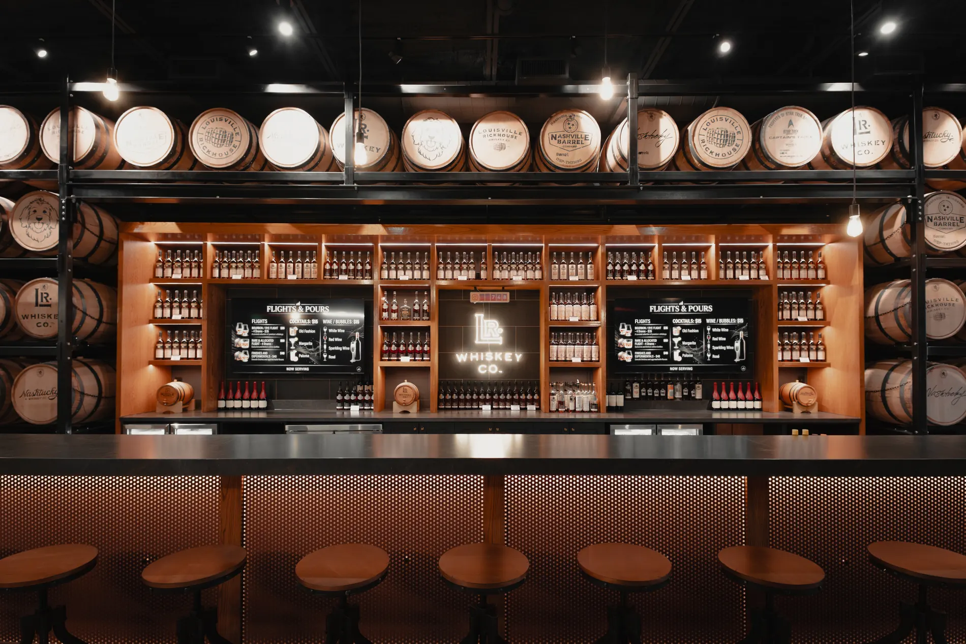 The tasting bar at Louisville Rickhouse — neon LR Whiskey Co. sign, bottle wall, and barrels overhead