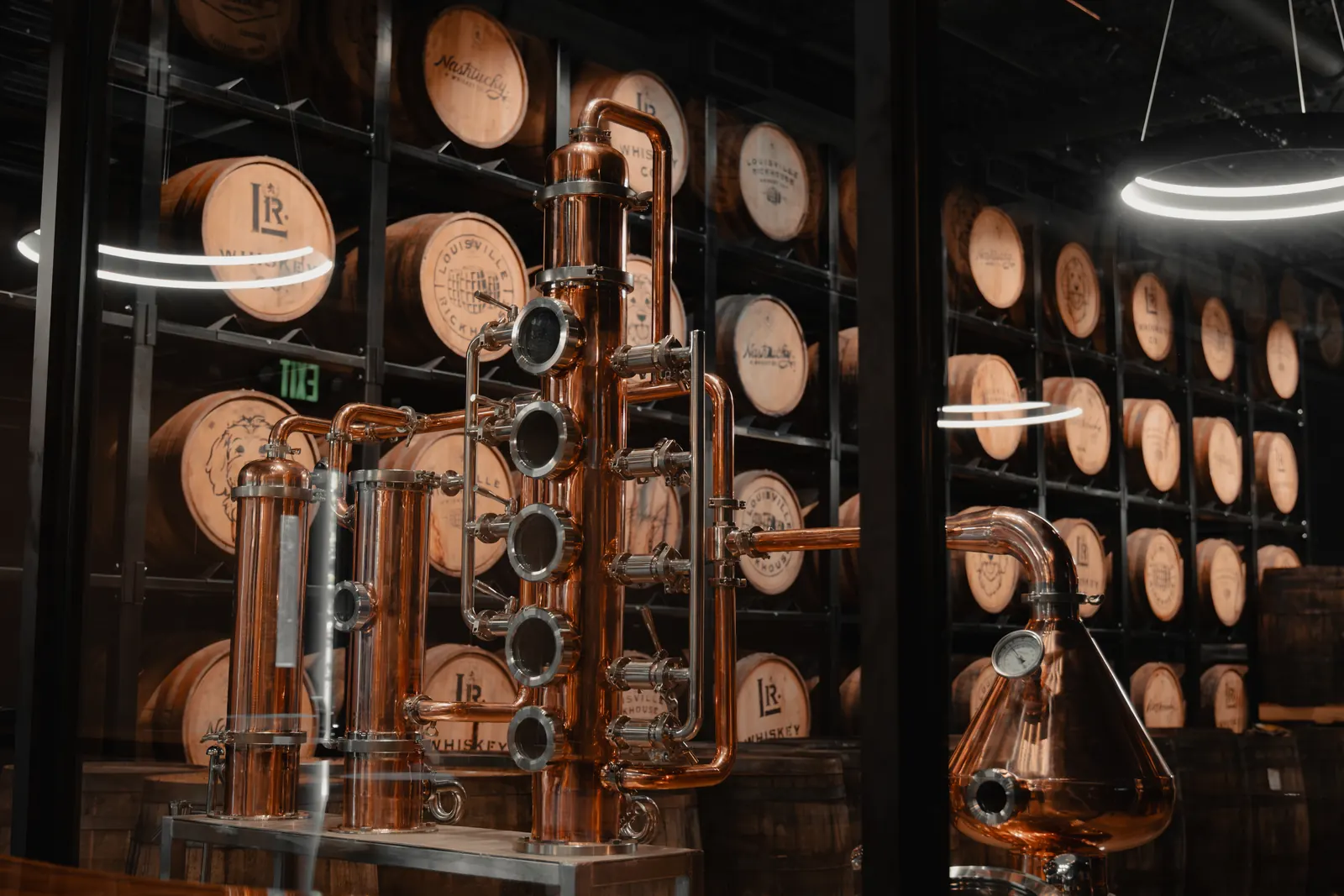 Copper still column framed by aging whiskey barrels at Louisville Rickhouse