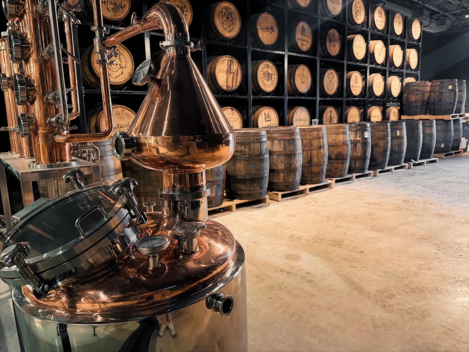 Copper pot still in front of racked Louisville Rickhouse barrels in the NuLu rickhouse